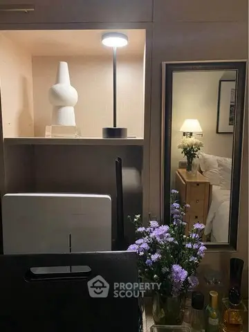 Cozy bedroom with elegant decor, featuring a stylish lamp, decorative vase, and fresh flowers for a serene ambiance.