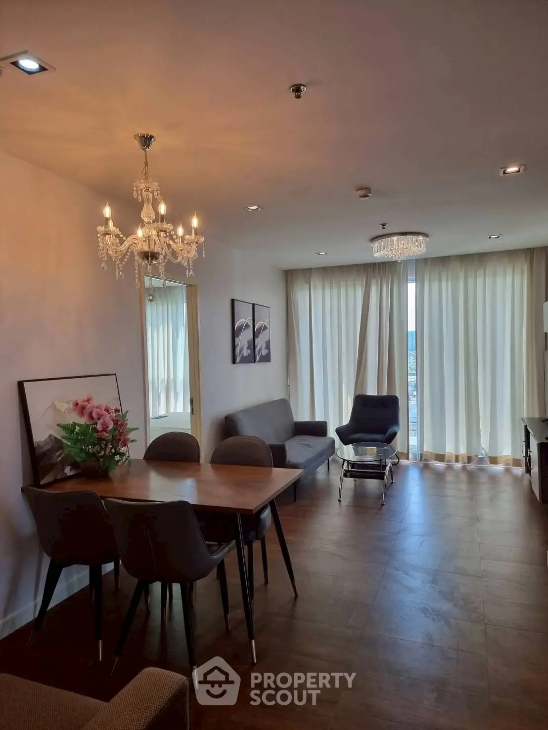 Elegant living room with chandelier, dining table, and floor-to-ceiling windows in modern apartment.