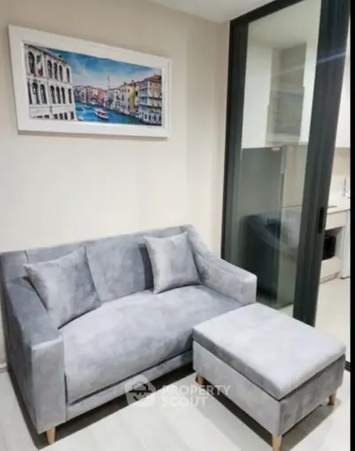 Modern living room with gray sofa and ottoman, large window, and stylish wall art.