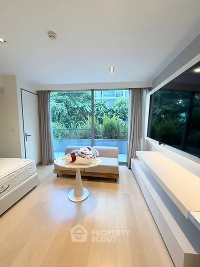 Modern living room with large window and garden view, featuring sleek furniture and natural light.