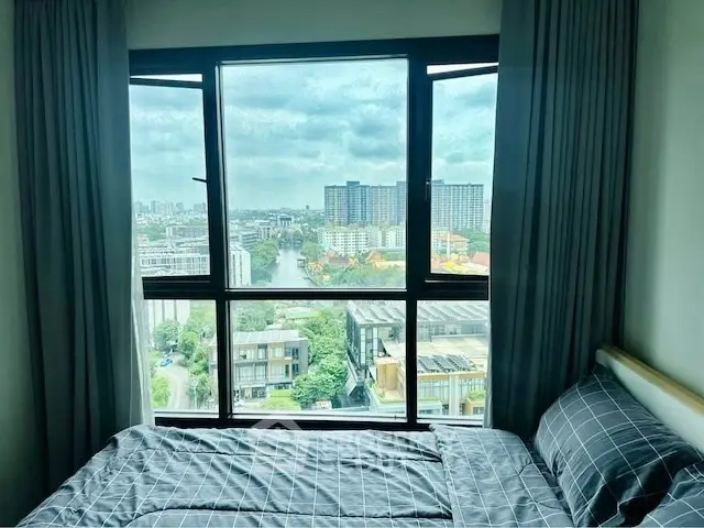 Stunning bedroom with panoramic city view from high-rise window, featuring modern decor and cozy bedding.