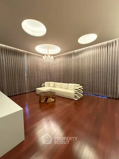 Luxurious living room with elegant chandelier and plush curtains, featuring polished hardwood floors and modern sofa.
