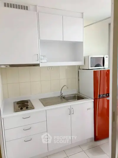 Compact kitchen with red fridge and white cabinets in modern apartment