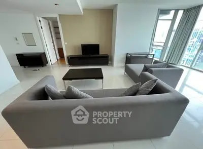 Spacious modern living room with sleek gray sofas and large windows offering city views.