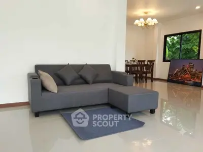 Modern living room with sleek gray sofa and dining area, featuring elegant lighting and lush garden view.
