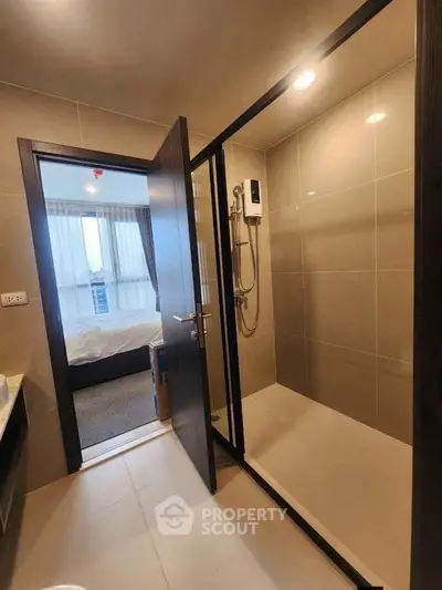 Modern bathroom with glass shower and view into a cozy bedroom with natural light.