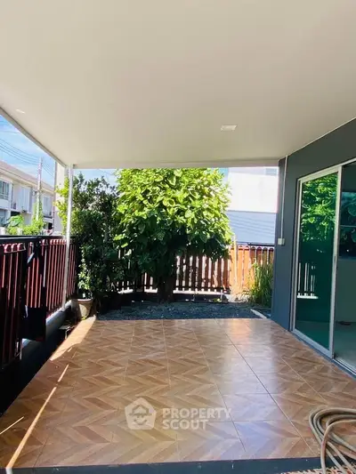 Spacious covered patio with tiled flooring and lush garden view, perfect for outdoor relaxation.