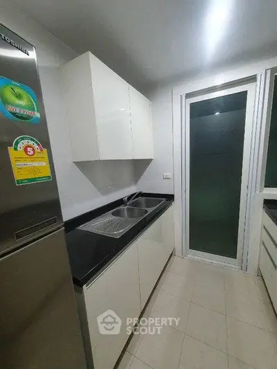 Modern kitchen with sleek cabinetry and stainless steel fridge in a compact layout.