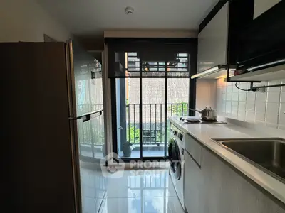 Modern kitchen with sleek appliances and balcony view, featuring washing machine and fridge.