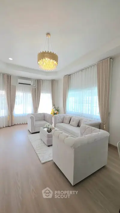 Elegant living room with plush sofas, chandelier, and large windows with sheer curtains.