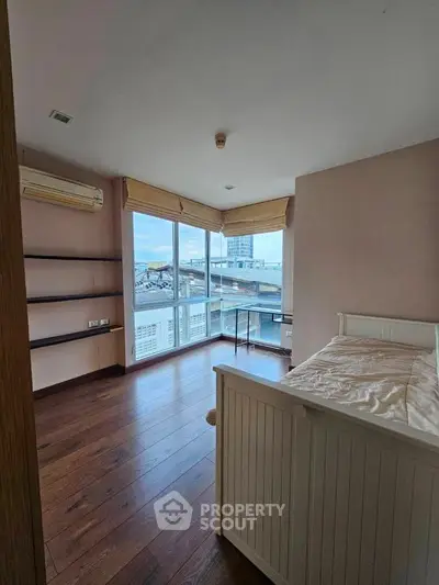 Spacious bedroom with large windows offering a stunning city view, featuring wooden floors and modern design.