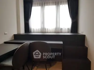 Modern study area with sleek desk and chairs, featuring large window and dark curtains.