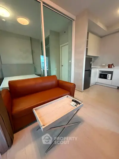 Modern studio apartment with sleek kitchen and cozy living area featuring a stylish brown sofa.