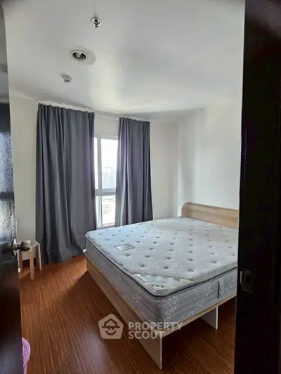 Cozy bedroom with large window and wooden flooring, featuring a comfortable bed and modern curtains.