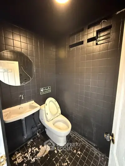 Modern black-tiled bathroom with round mirror and white fixtures