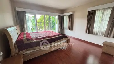 Spacious bedroom with large windows and wooden flooring, offering a serene garden view.
