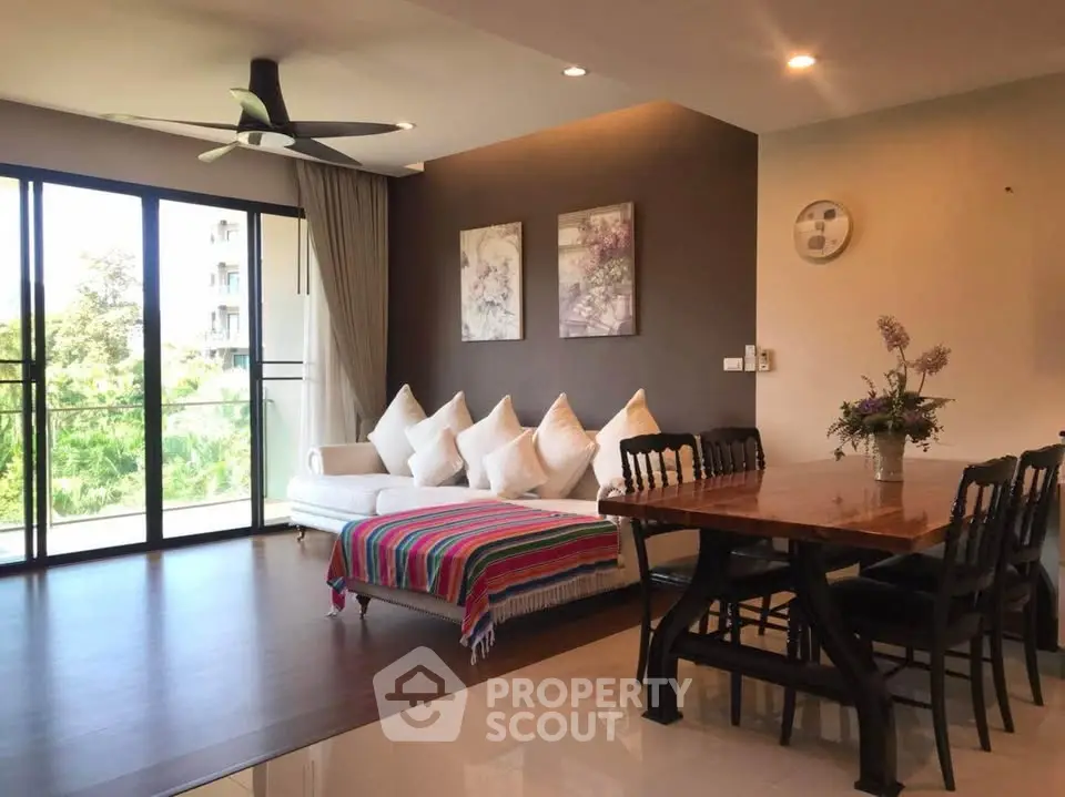 Spacious living room with modern decor and large windows offering natural light and greenery views.