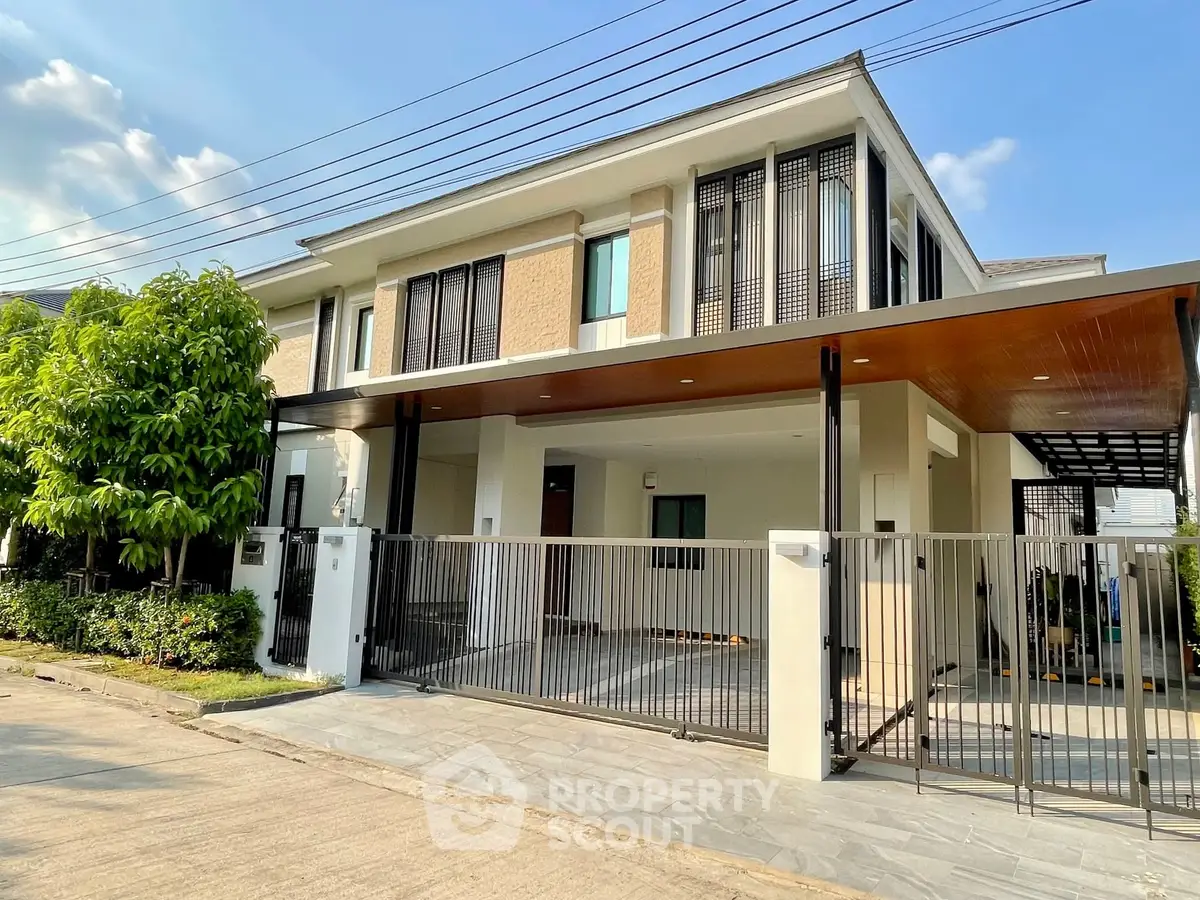Modern two-story house with gated entrance and carport in a sunny neighborhood.