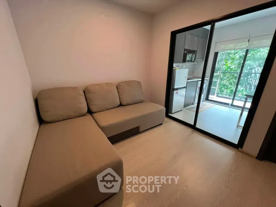 Modern living room with cozy sofa and view into kitchen with balcony access