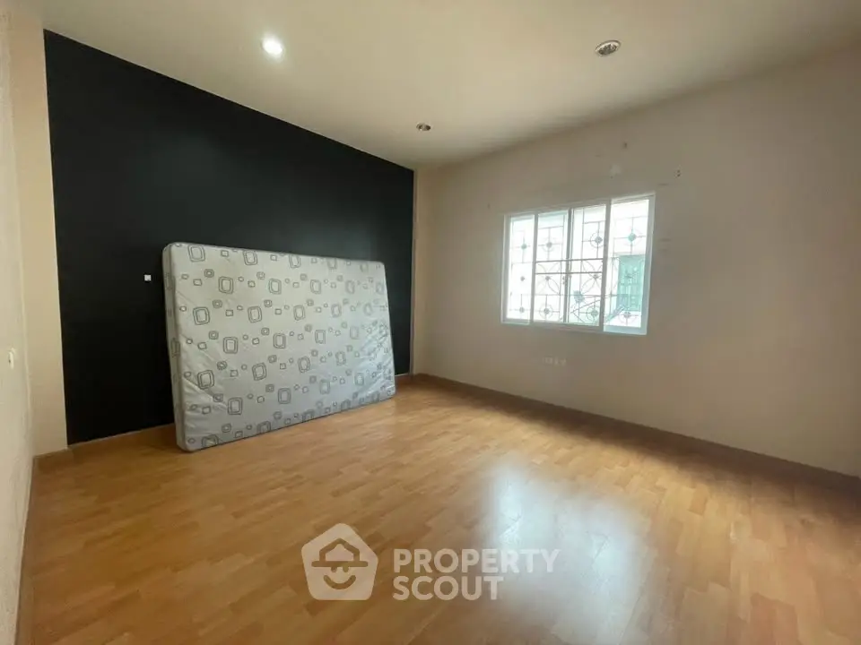 Spacious empty bedroom with wooden flooring and large window, ready for customization.