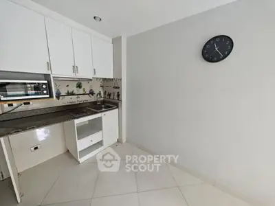 Compact kitchen space with white cabinets and wall clock, ideal for small apartments.
