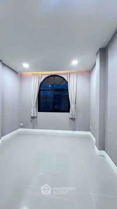 Spacious empty room with elegant arched window and modern lighting, perfect for customization.