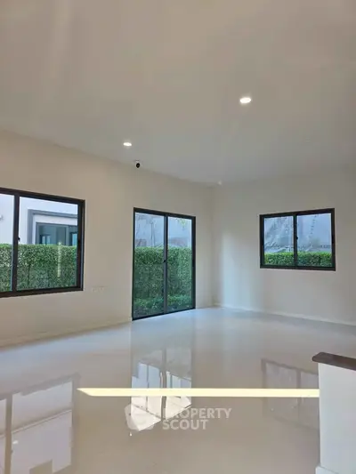 Spacious modern living room with large windows and glossy floors, offering abundant natural light and garden views.