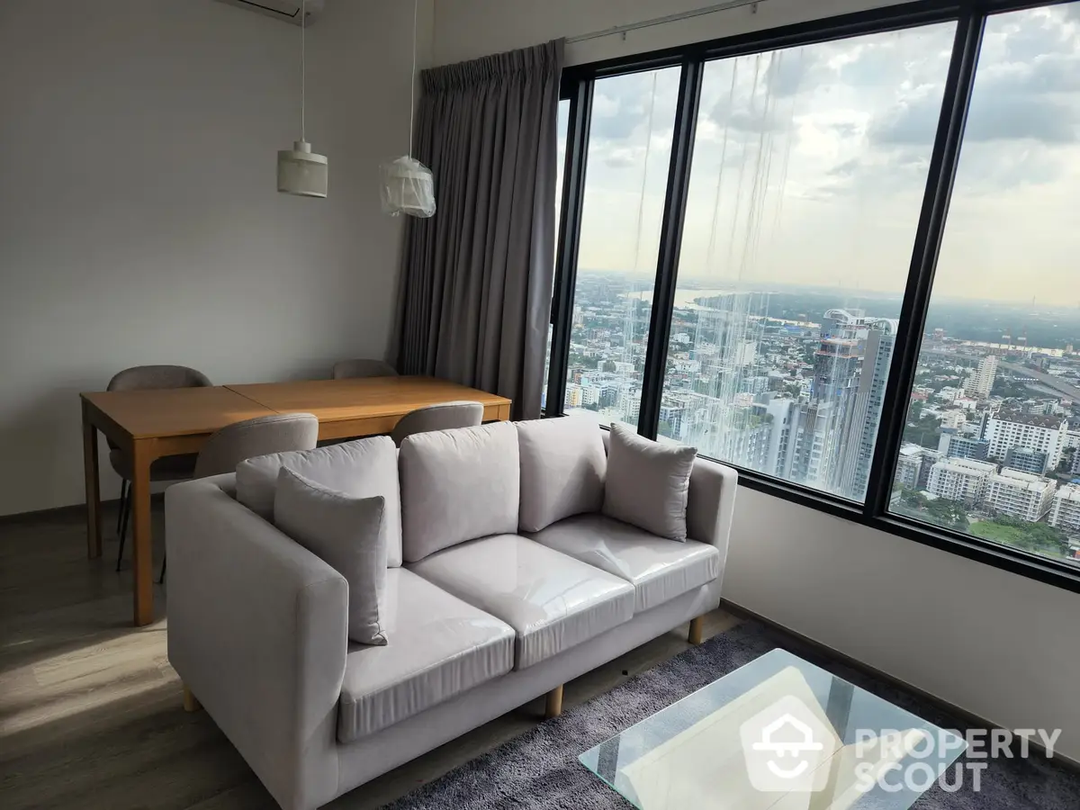 Spacious high-rise living room with modern furnishings, floor-to-ceiling windows offering panoramic city views, and a cozy, elegant ambiance.