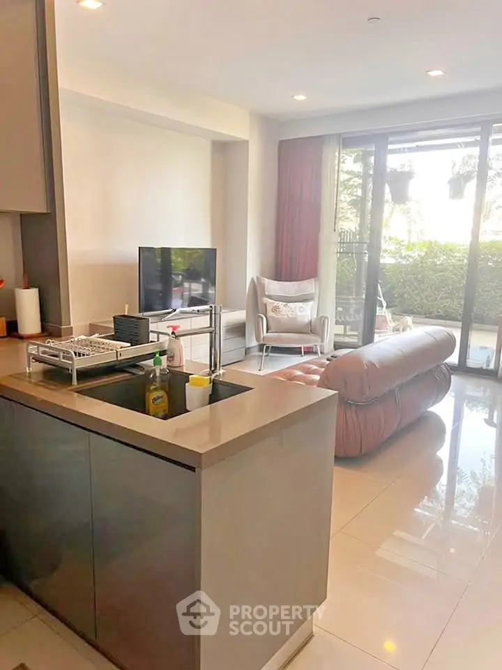Modern living room with open kitchen and garden view, featuring sleek furniture and natural light.
