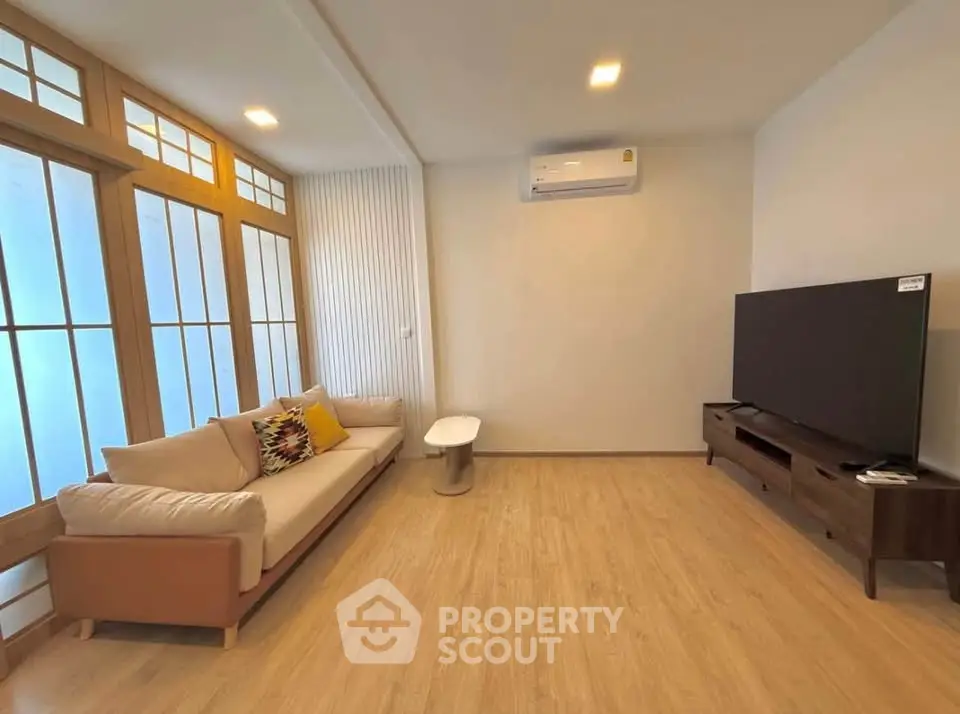 Modern living room with wooden flooring, large TV, and stylish sofa in bright natural light.