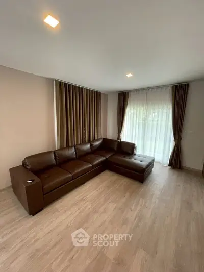 Spacious living room with elegant brown leather sectional sofa and large windows with curtains.