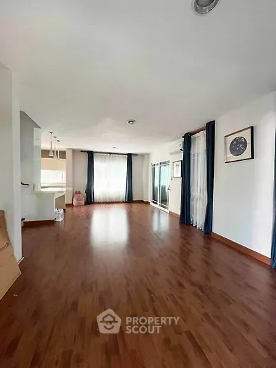 Spacious living room with wooden flooring and large windows for natural light.