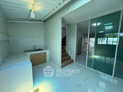 Modern kitchen with sleek white countertops and open layout, featuring a staircase and glass sliding door.
