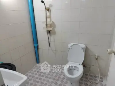 Compact bathroom with tiled walls and floor, featuring a toilet and shower area.