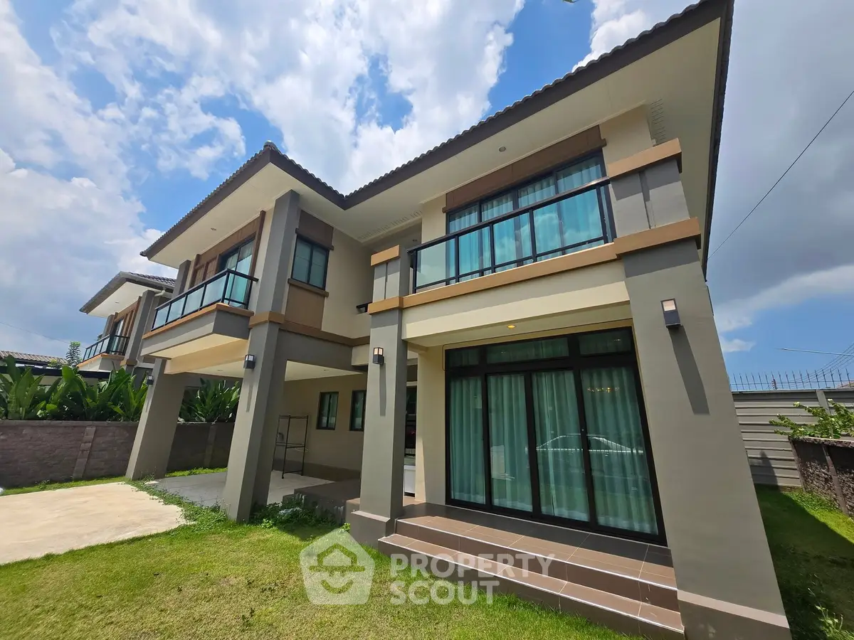Modern two-story house with large windows and manicured lawn under a bright blue sky.