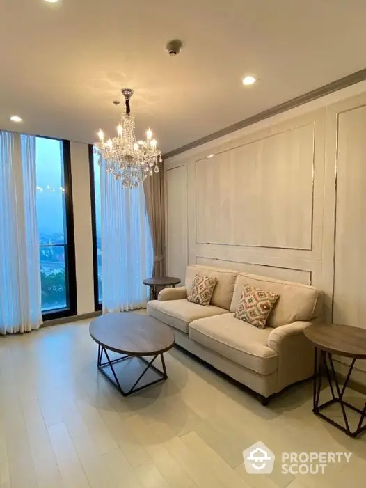 Elegant living room with a luxurious crystal chandelier, modern furniture, and floor-to-ceiling windows offering ample natural light.