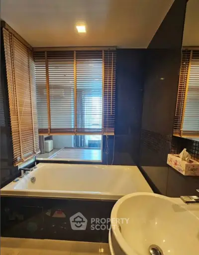 Luxurious bathroom with large bathtub and modern fixtures, featuring elegant wooden blinds and ambient lighting.