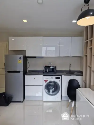 Modern kitchen with sleek cabinets, washing machine, and stainless steel fridge in compact layout.