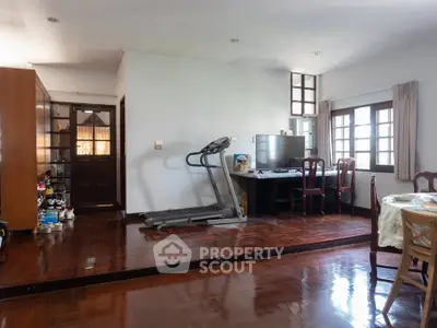 Spacious living room with treadmill and dining area, featuring wooden flooring and large windows.