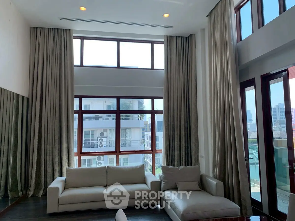 Spacious living room with high ceilings and large windows offering city views.