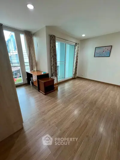 Spacious room with wooden flooring and large windows offering natural light, ideal for versatile living space.