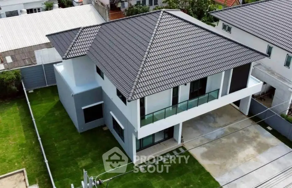 Modern two-story house with sleek design and spacious lawn, featuring a stylish roof and large windows.
