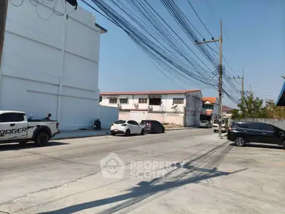 Street view with parked cars and residential buildings under clear blue sky.