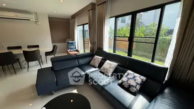 Spacious living room with modern black leather sofa and large windows overlooking garden.
