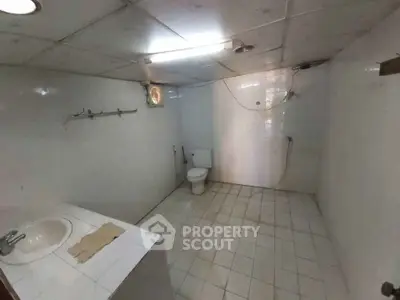 Spacious bathroom with tiled flooring and ceiling, featuring a toilet and sink.