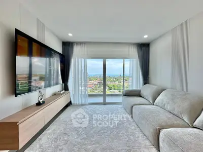 Modern living room with large TV and stunning city view through floor-to-ceiling windows.