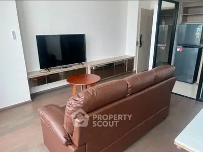 Modern living room with brown leather sofa, flat-screen TV, and sleek kitchen area.