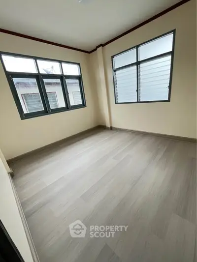 Spacious empty room with large windows and light wood flooring, perfect for customization.