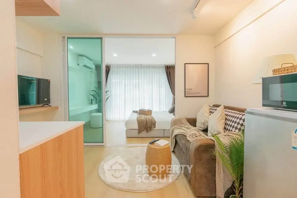 Modern studio apartment with cozy living area and stylish bedroom separated by glass partition.