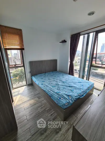 Modern bedroom with large windows and city view, featuring wooden flooring and stylish decor.